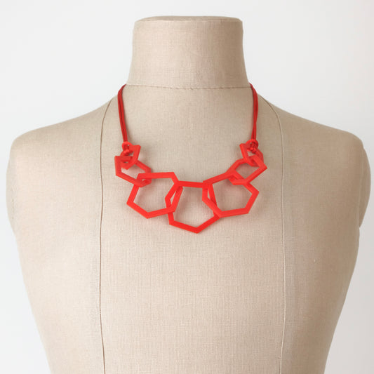 Red geometric necklace on a mannequin bust against a white background