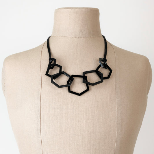 Black geometric necklace on a mannequin bust against a white background