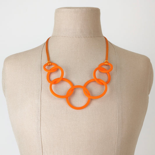 Orange necklace on a mannequin bust against a plain background