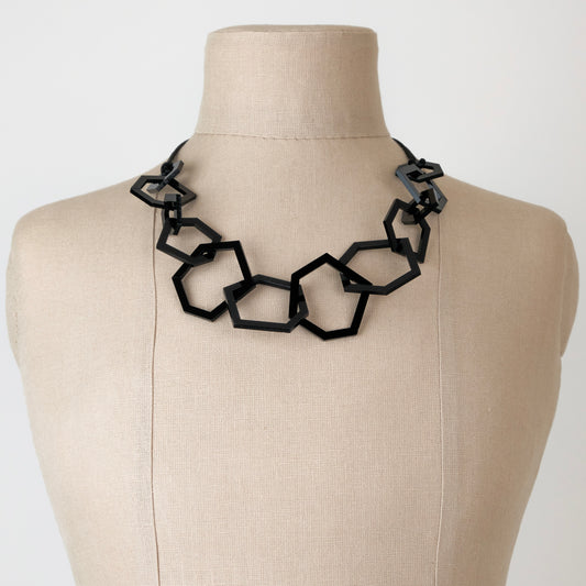 Black geomtric necklace on a mannequin against a white background