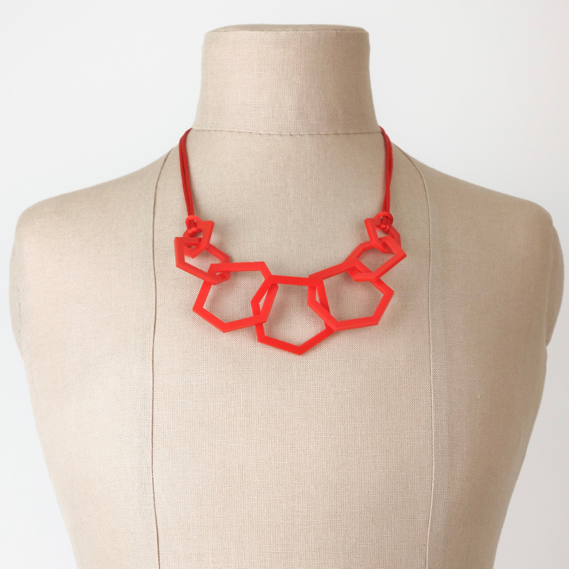 Red geometric necklace on a mannequin bust against a white background