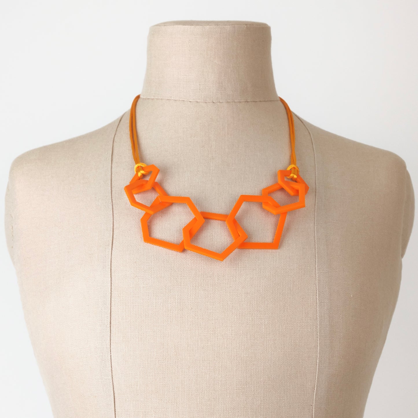 Orange geometric necklace on a mannequin bust against a white background