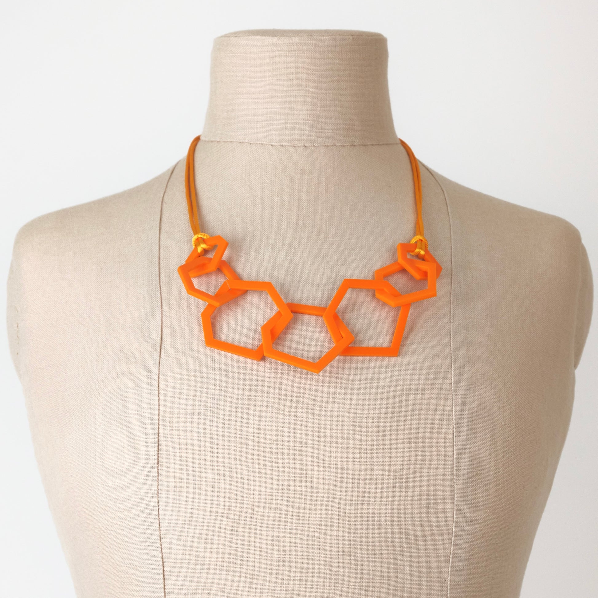 Orange geometric necklace on a mannequin bust against a white background
