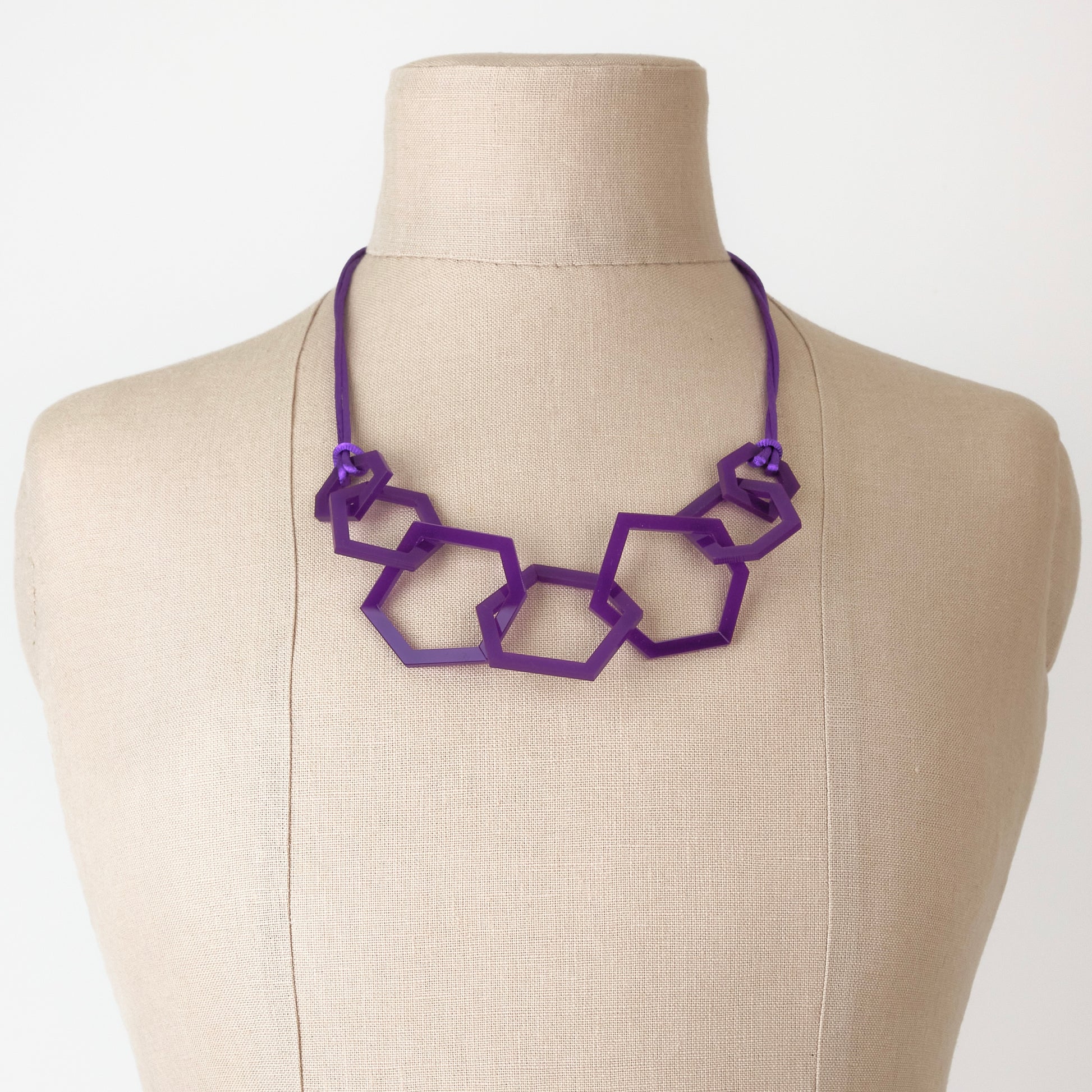 Purple geometric acrylic necklace on a mannequin bust against a white background