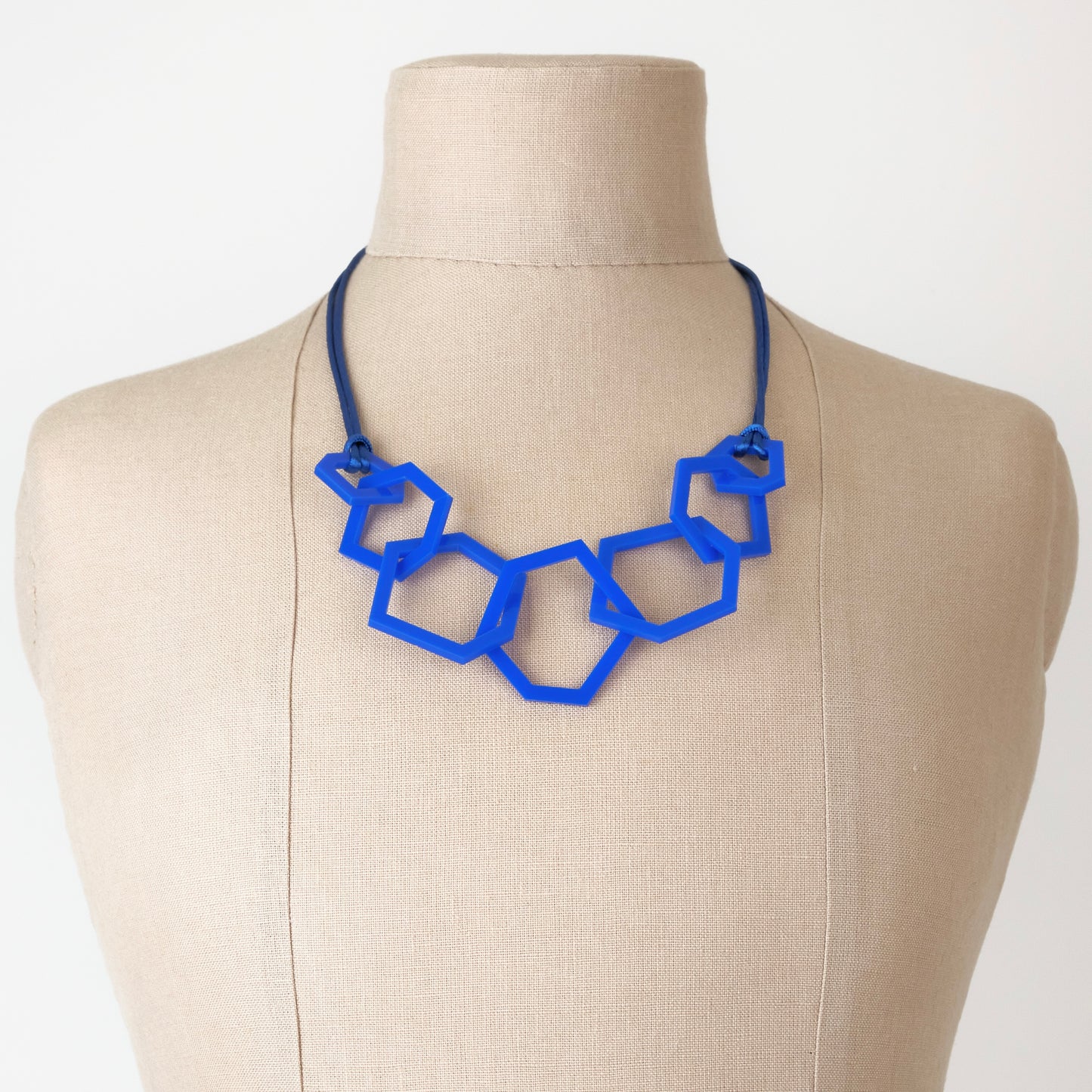 Blue geometric necklace on a mannequin bust against a white background