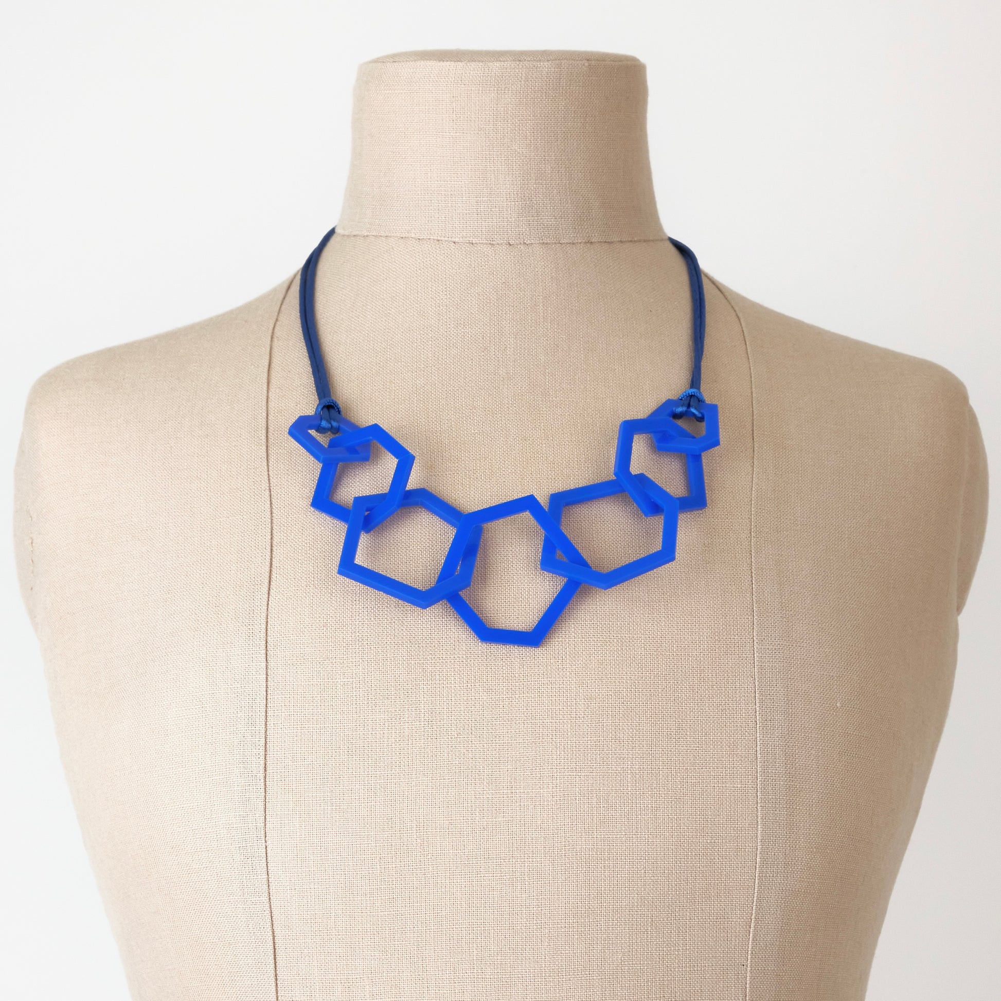 Blue geometric necklace on a mannequin bust against a white background