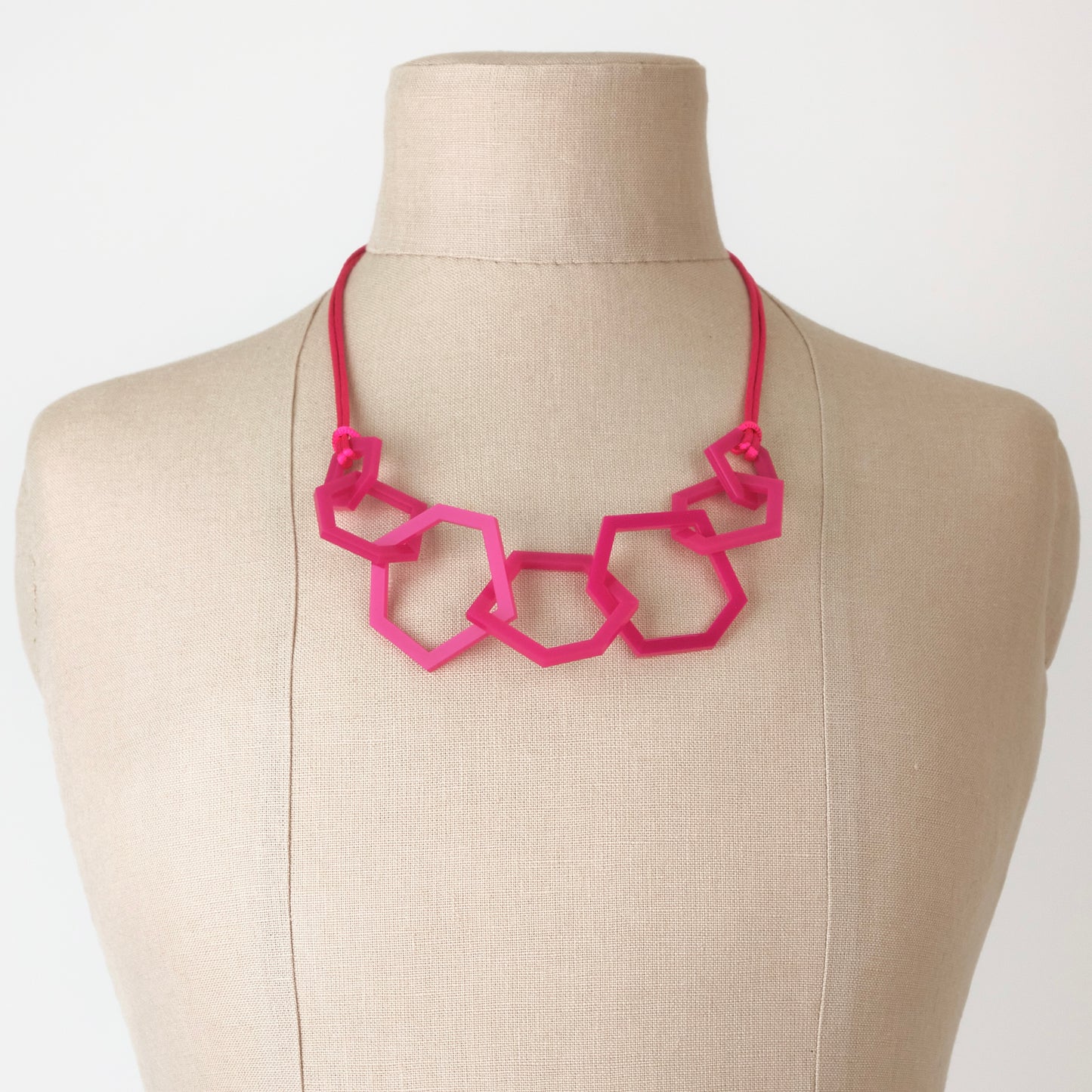 Fuchsia Pink geometric necklace on a mannequin with a plain background