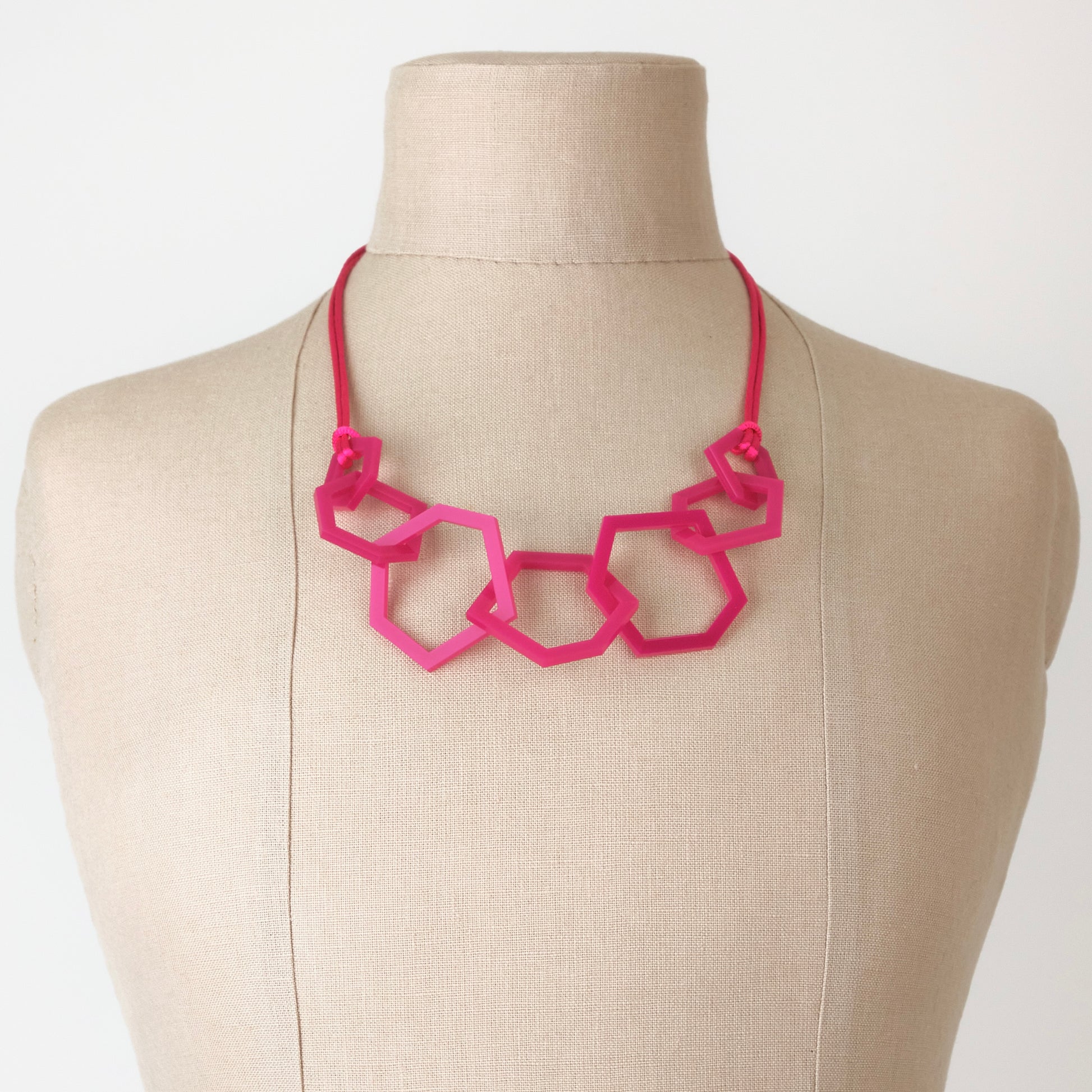 Fuchsia Pink geometric necklace on a mannequin with a plain background