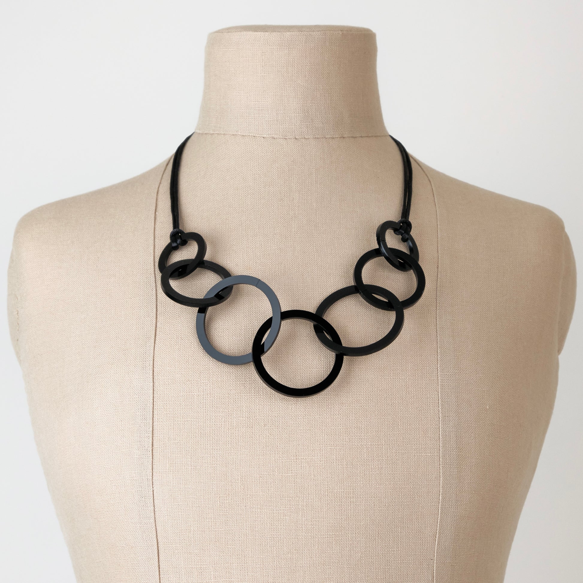 Necklace with black circular links on a mannequin bust against a white background