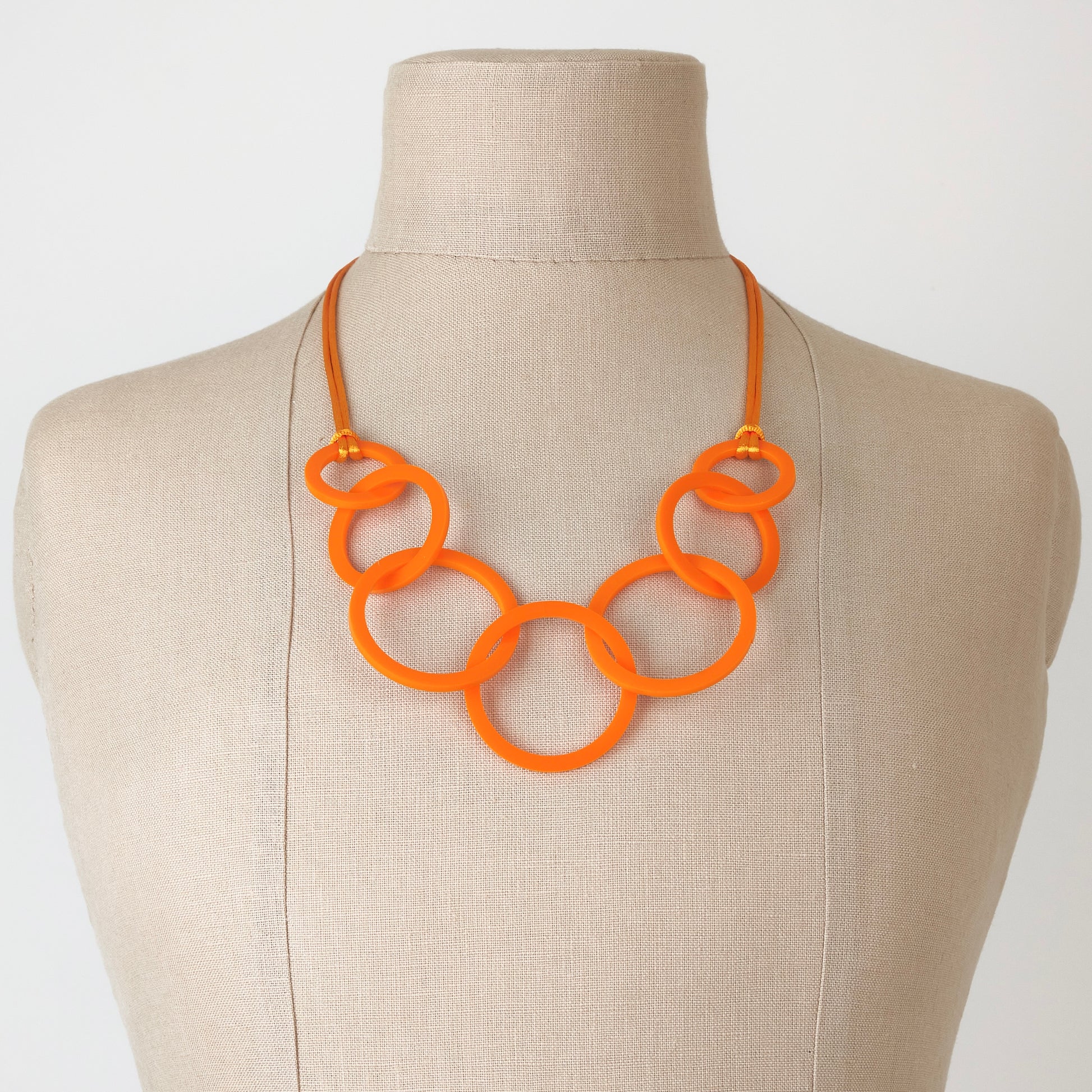 Orange necklace on a mannequin bust against a plain background