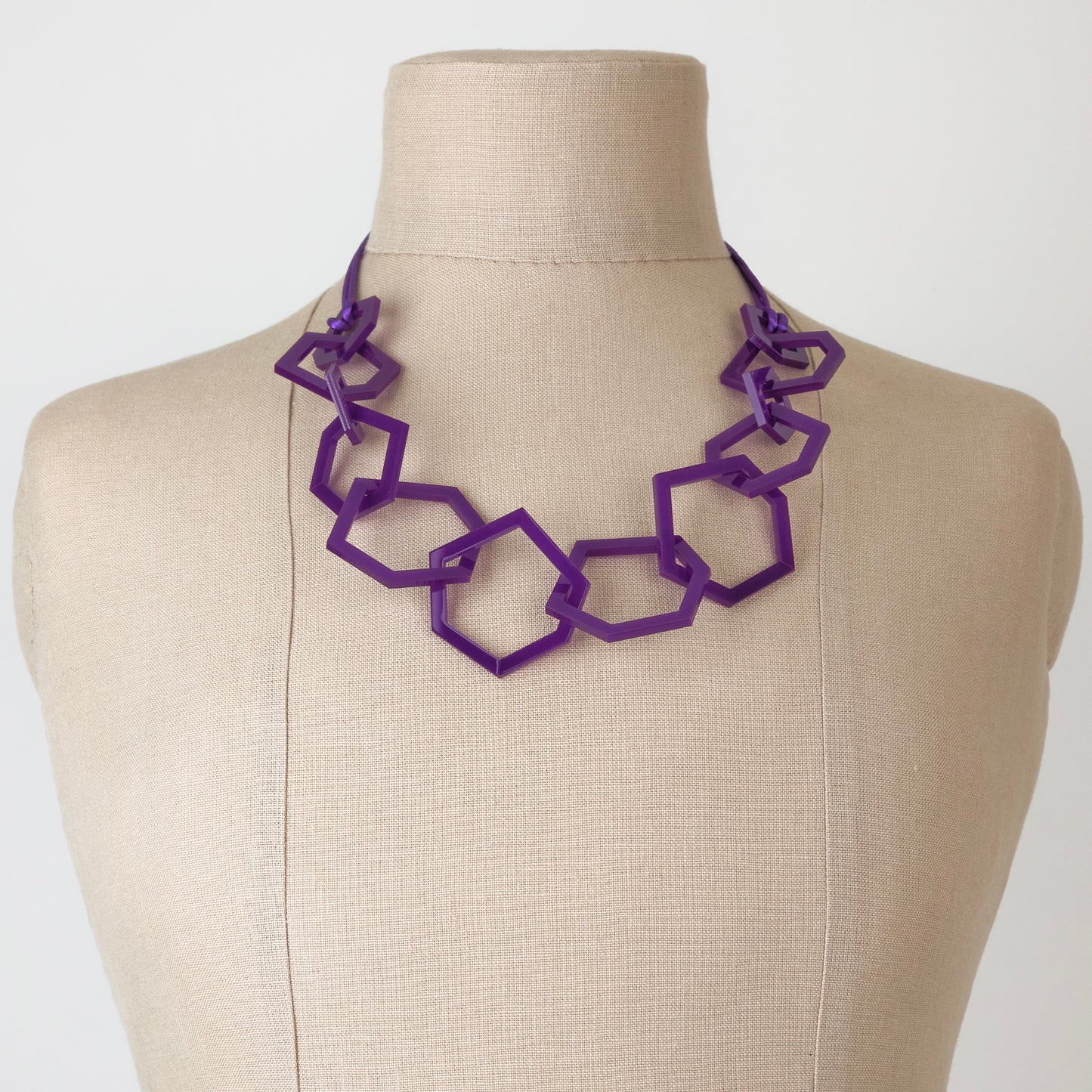 Purple geometric necklace on a mannequin bust against a white background