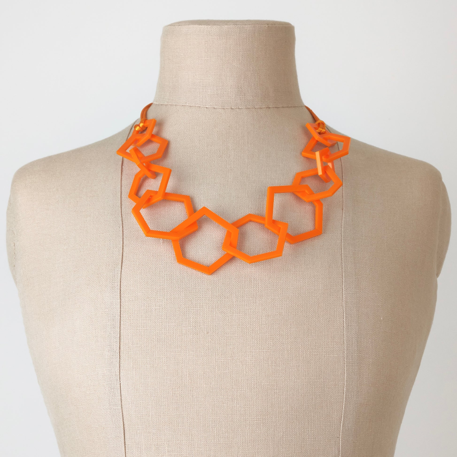 Orange geometric necklace on a mannequin bust against a white background