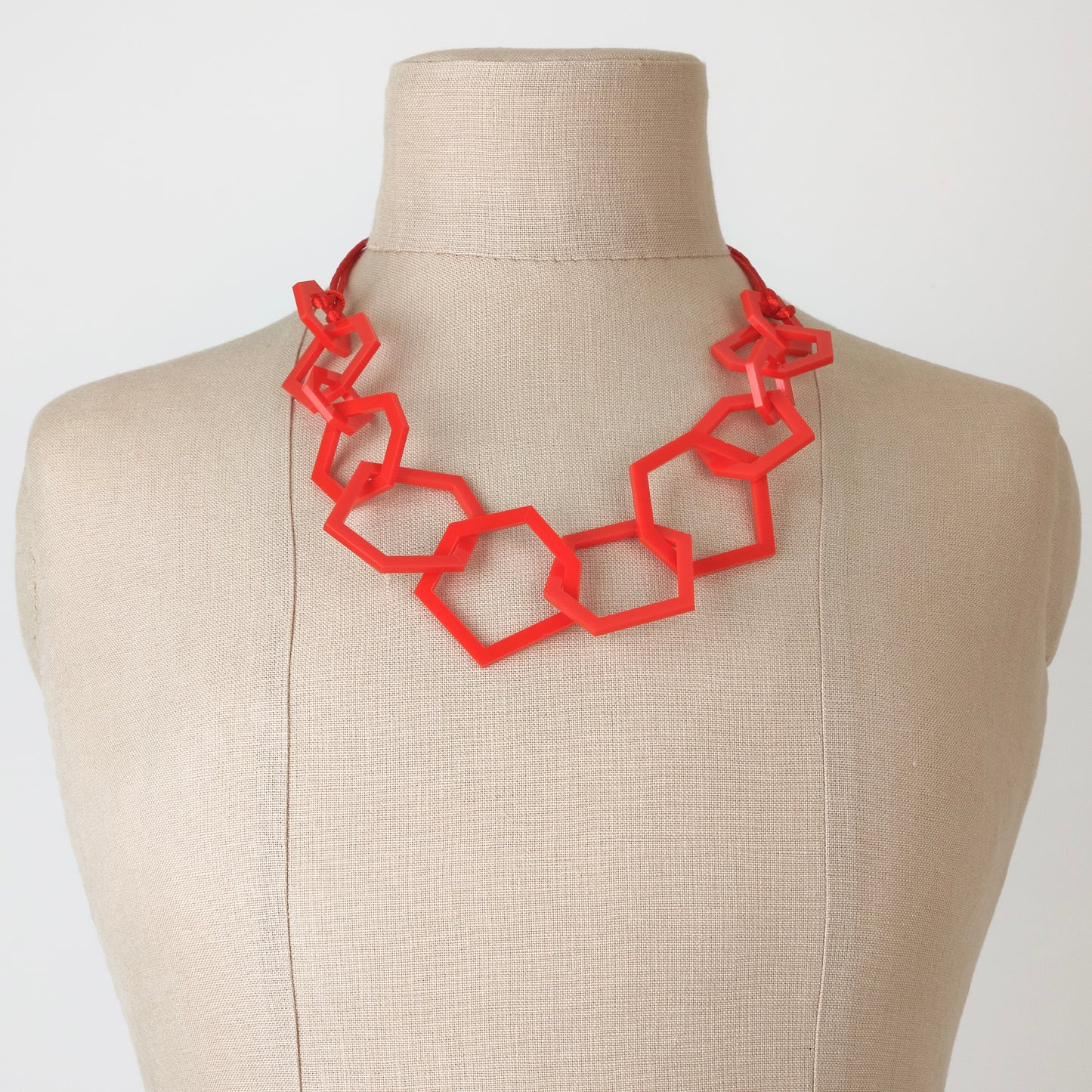 Red geometric necklace on a mannequin with a plain background