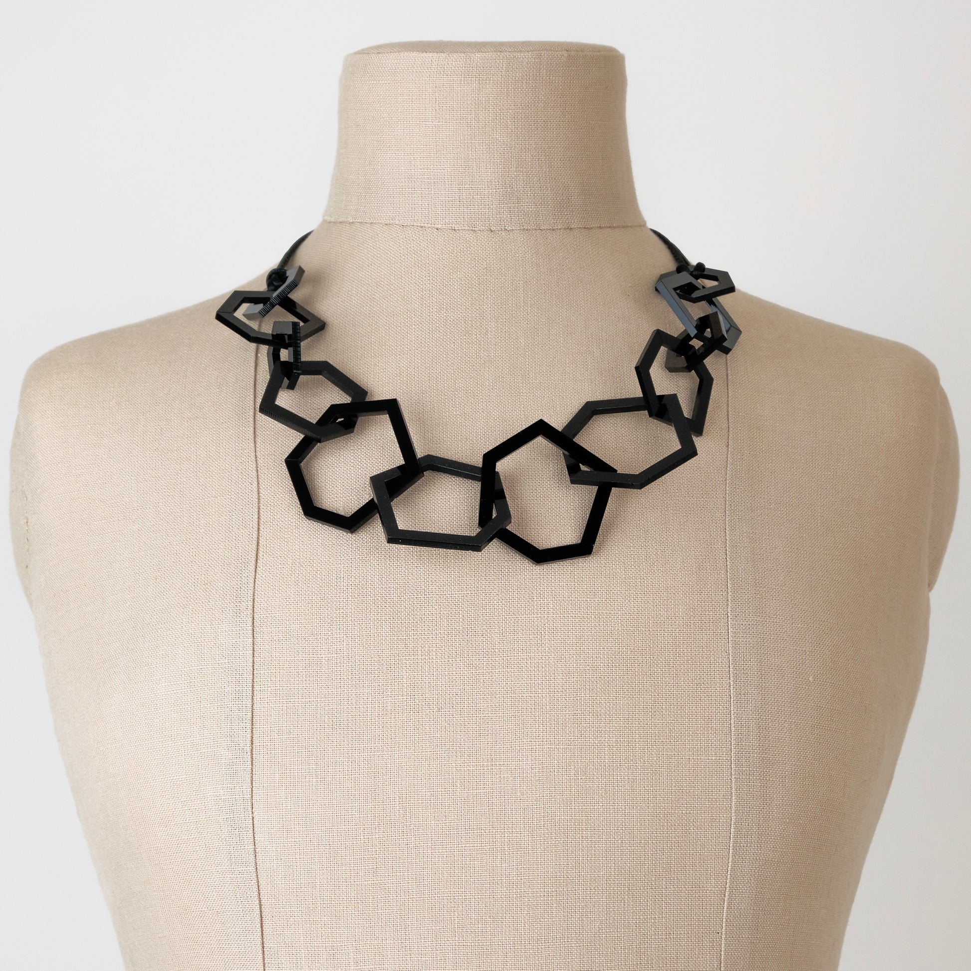Black geomtric necklace on a mannequin against a white background