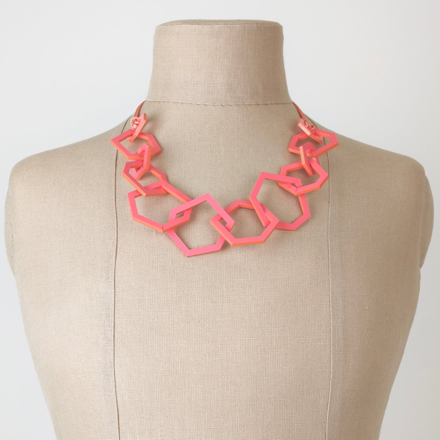 Coral pink geometric necklace on a mannequin bust against a white background