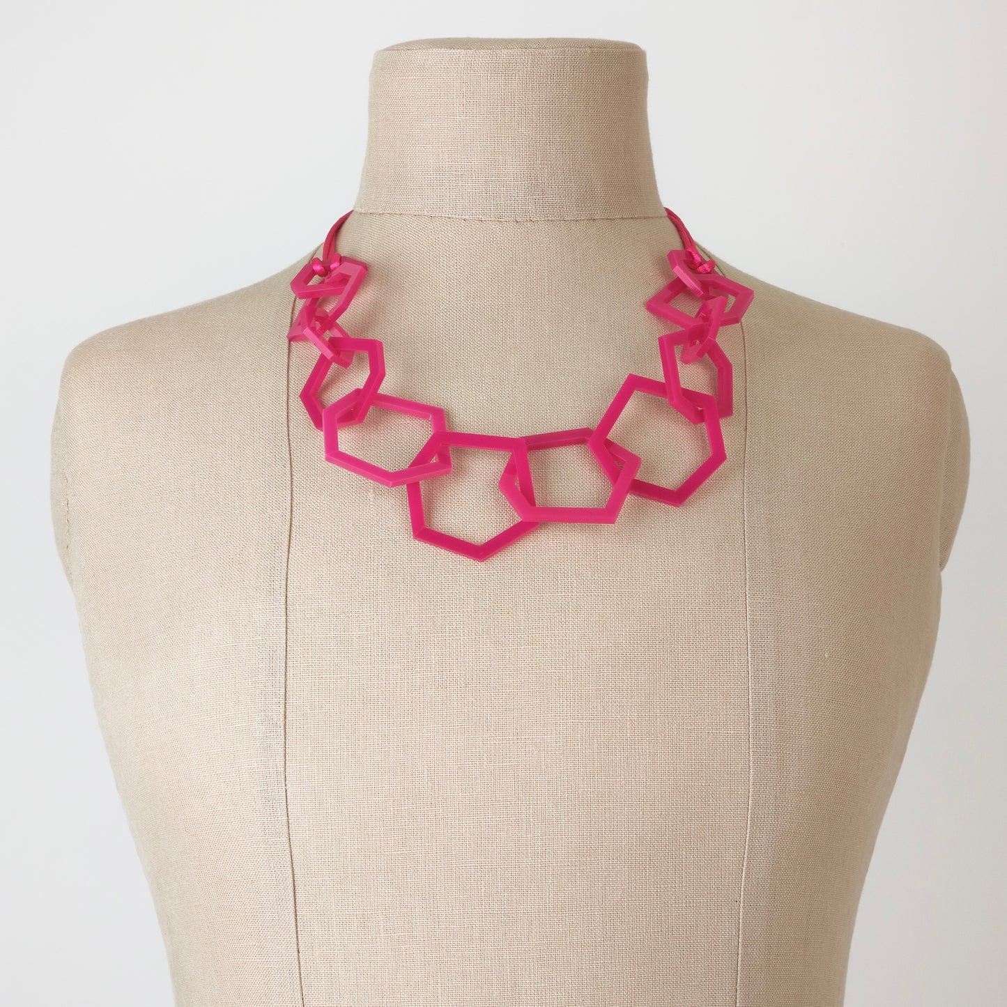Fuchsia Pink geometric necklace on a mannequin bust against a white background