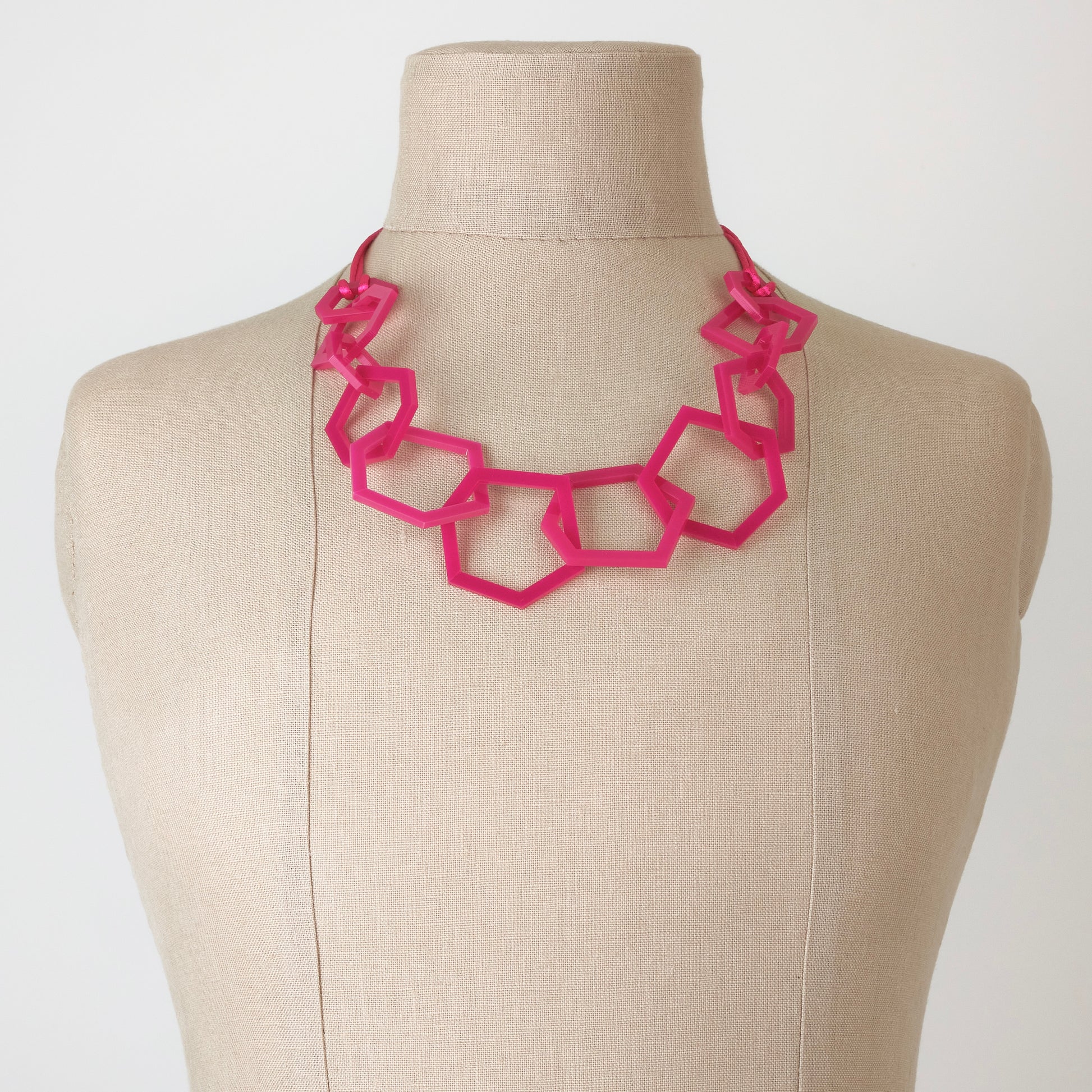 Fuchsia Pink geometric necklace on a mannequin bust against a white background