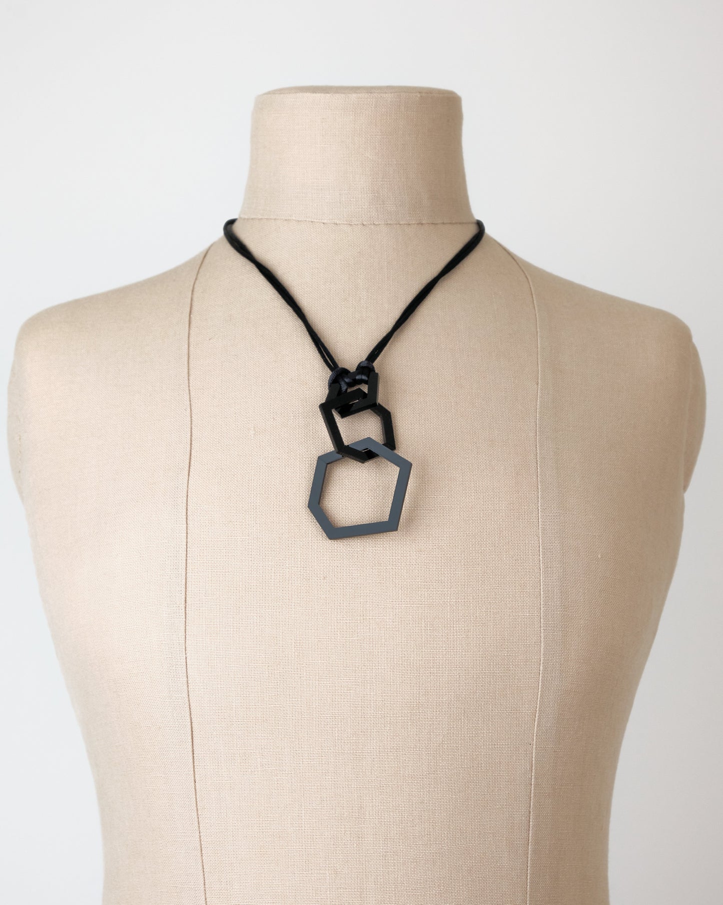 Necklace with a hexagonal pendant on a mannequin bust against a plain background