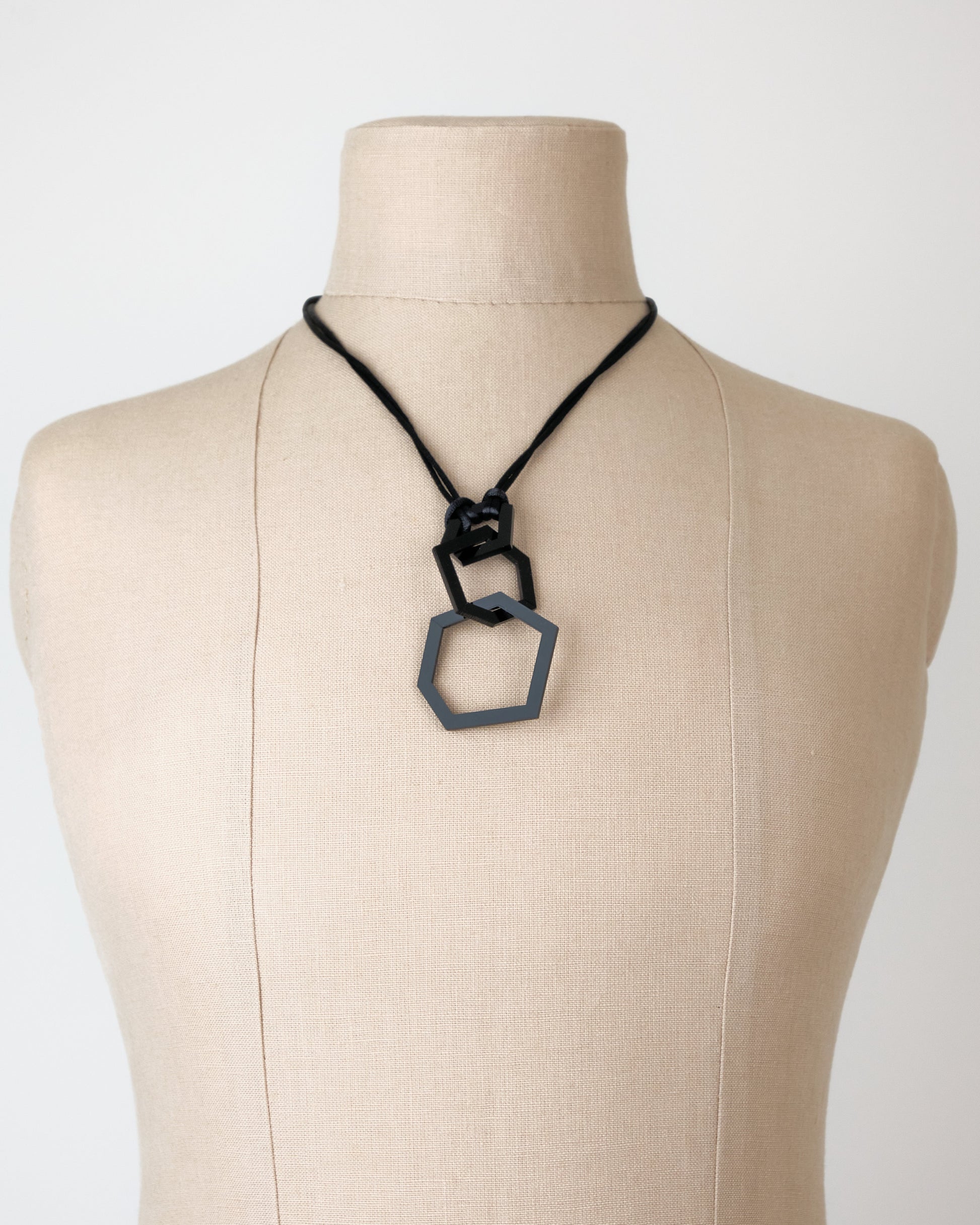 Necklace with a hexagonal pendant on a mannequin bust against a plain background