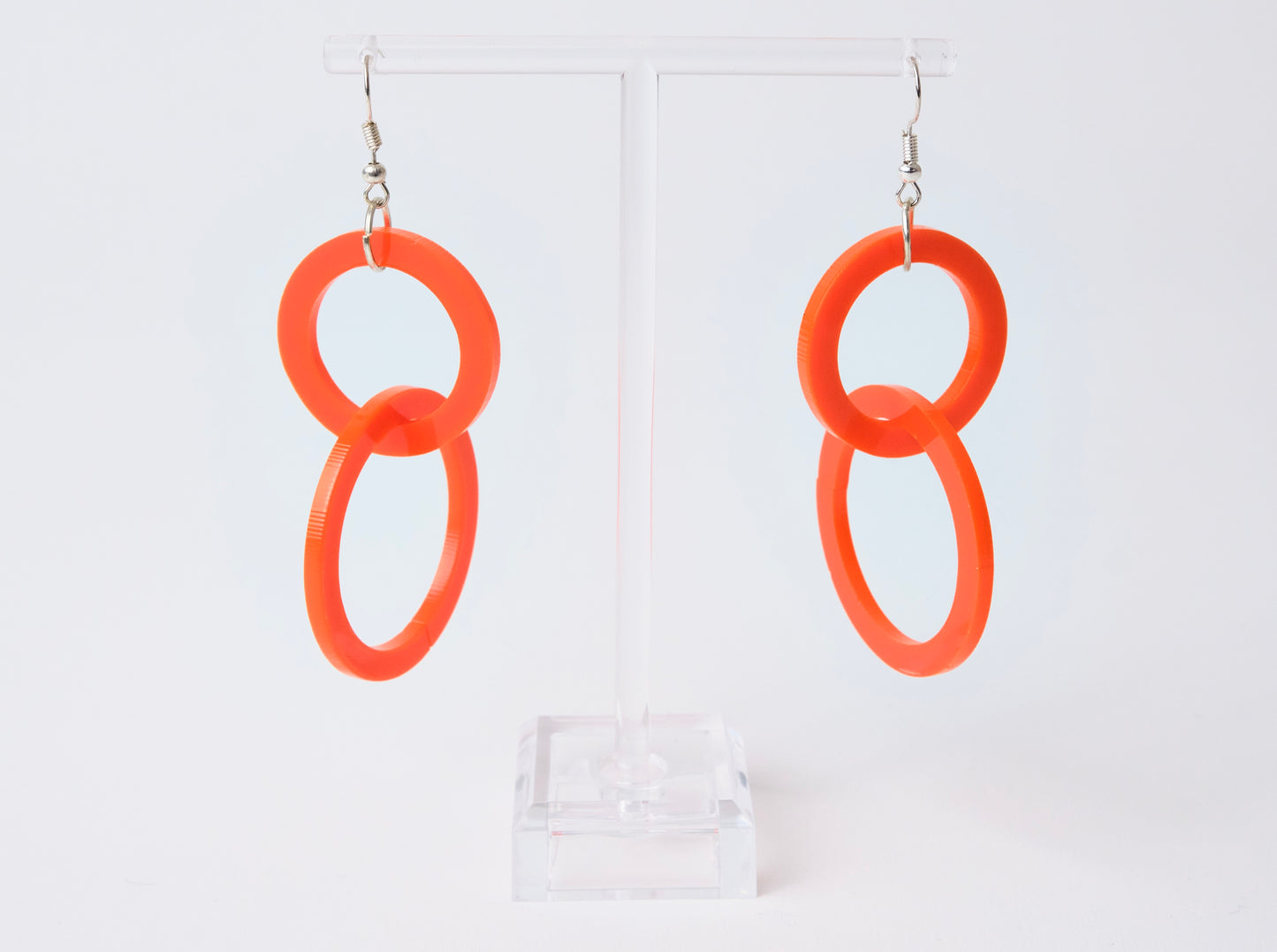 Orange hoop earrings on a clear stand against a white background