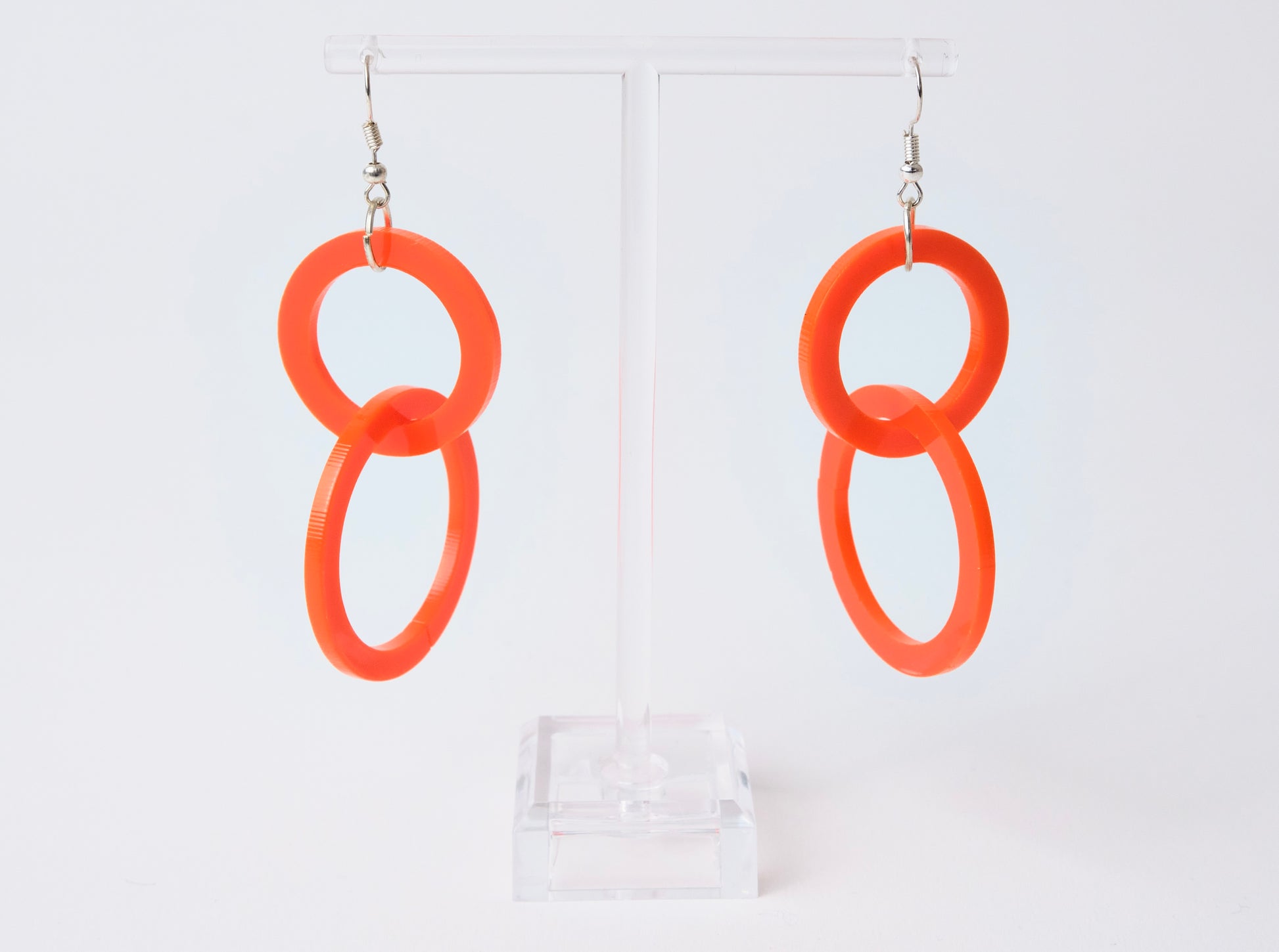 Orange hoop earrings on a clear stand against a white background