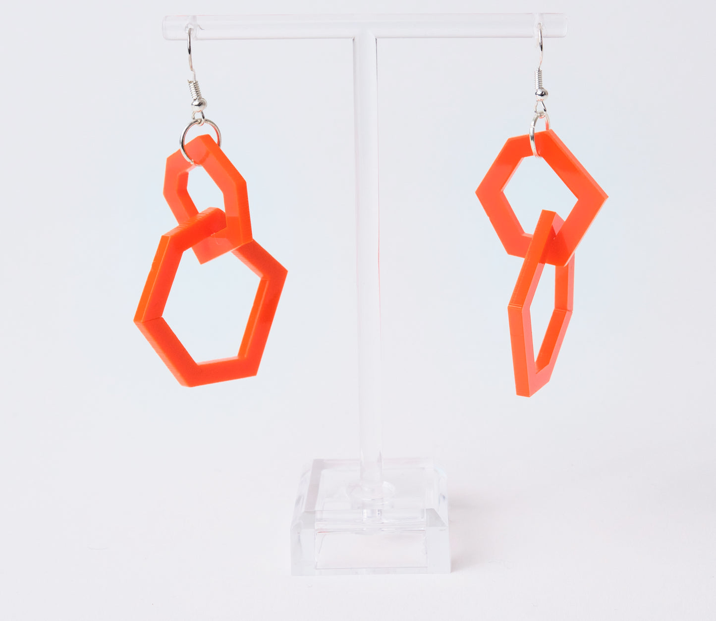 orange geometric earrings on a clear stand against a white background