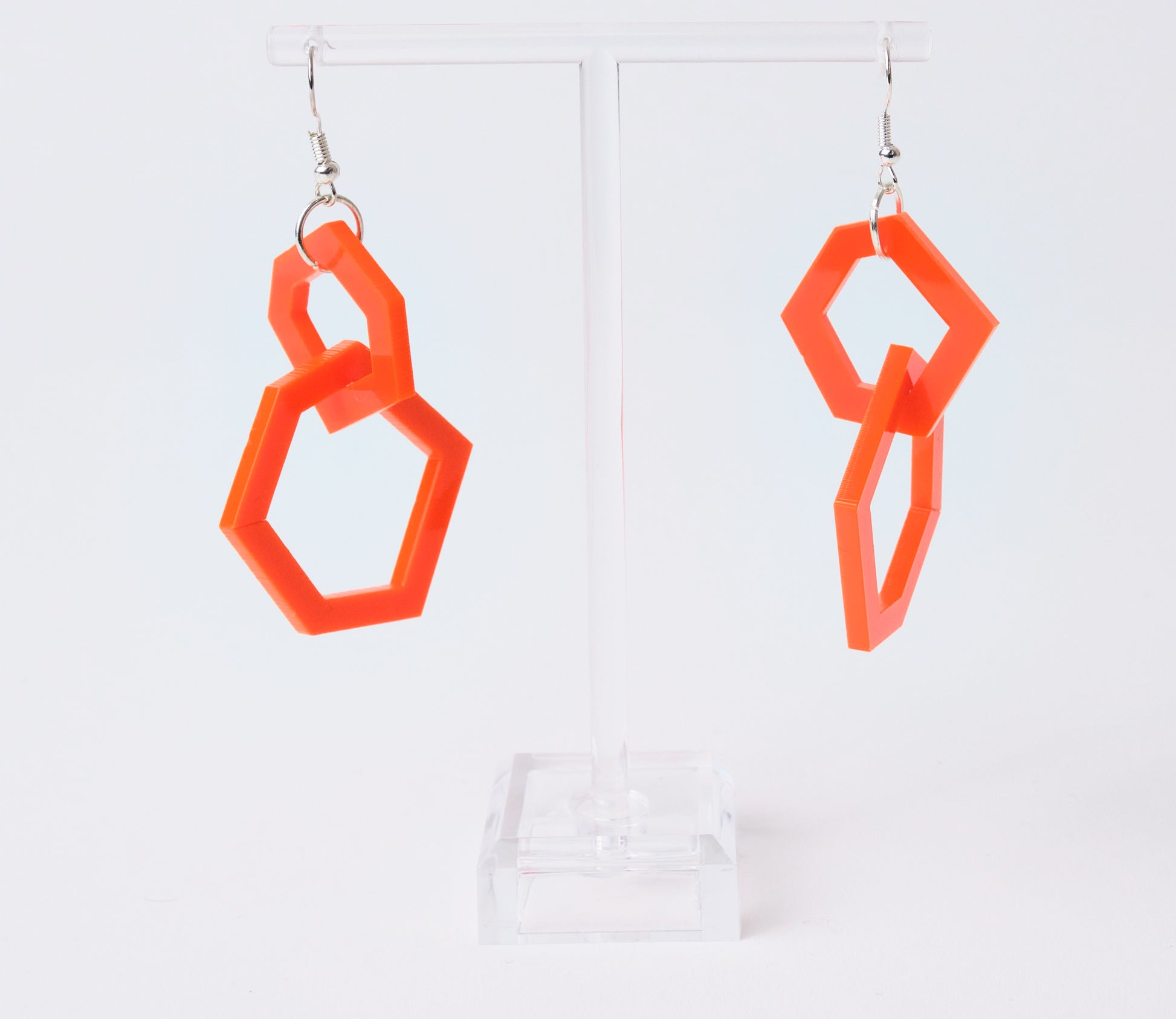 orange geometric earrings on a clear stand against a white background